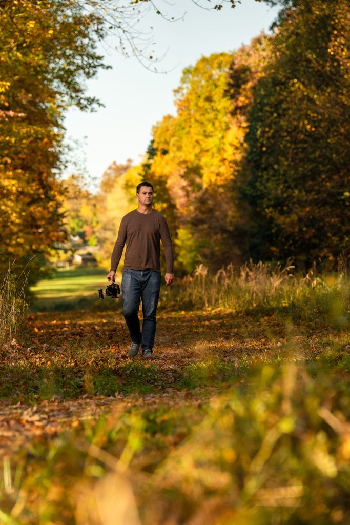 Joe walking in autumn woods holding a camera