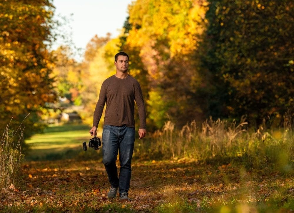 Joe walking in autumn woods holding a camera